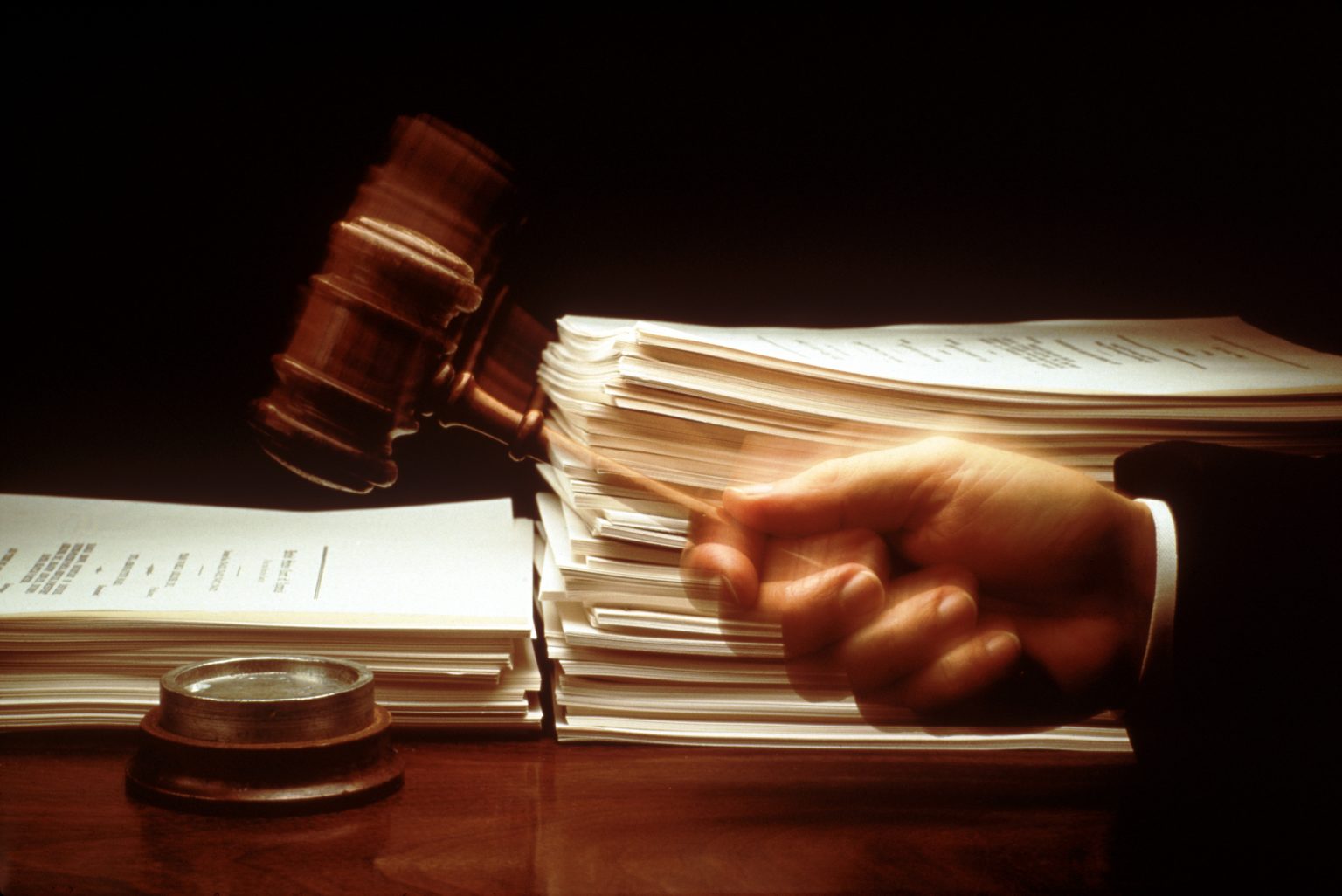 Hand with black sleeve holding a gavel, piles of documents
